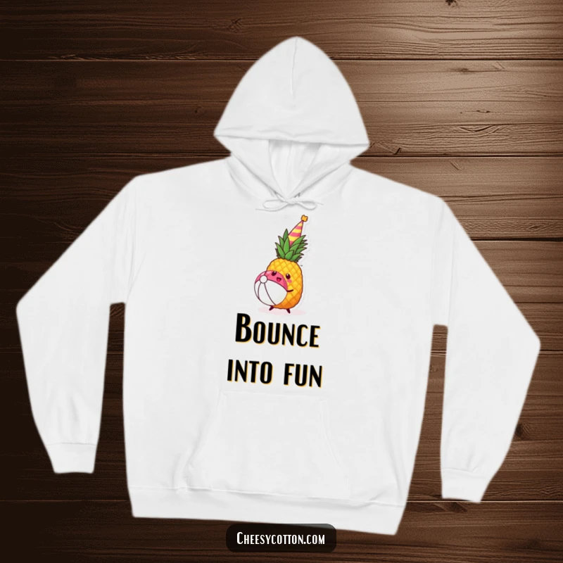 Funny kawaii pineapple with a party hat bouncing a beach ball on a cozy hoodie, evoking warmth.